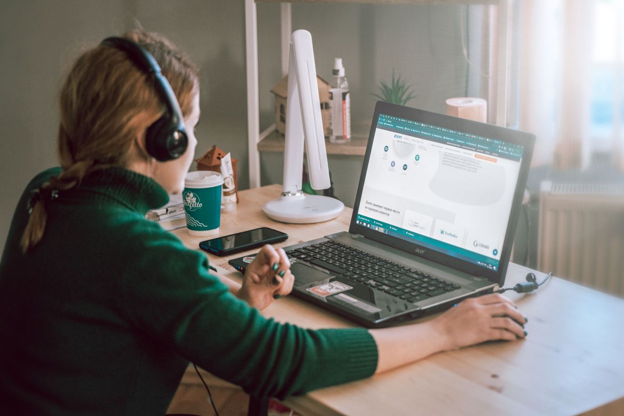 Woman using a laptop at a home office, focused on her work with headphones on.