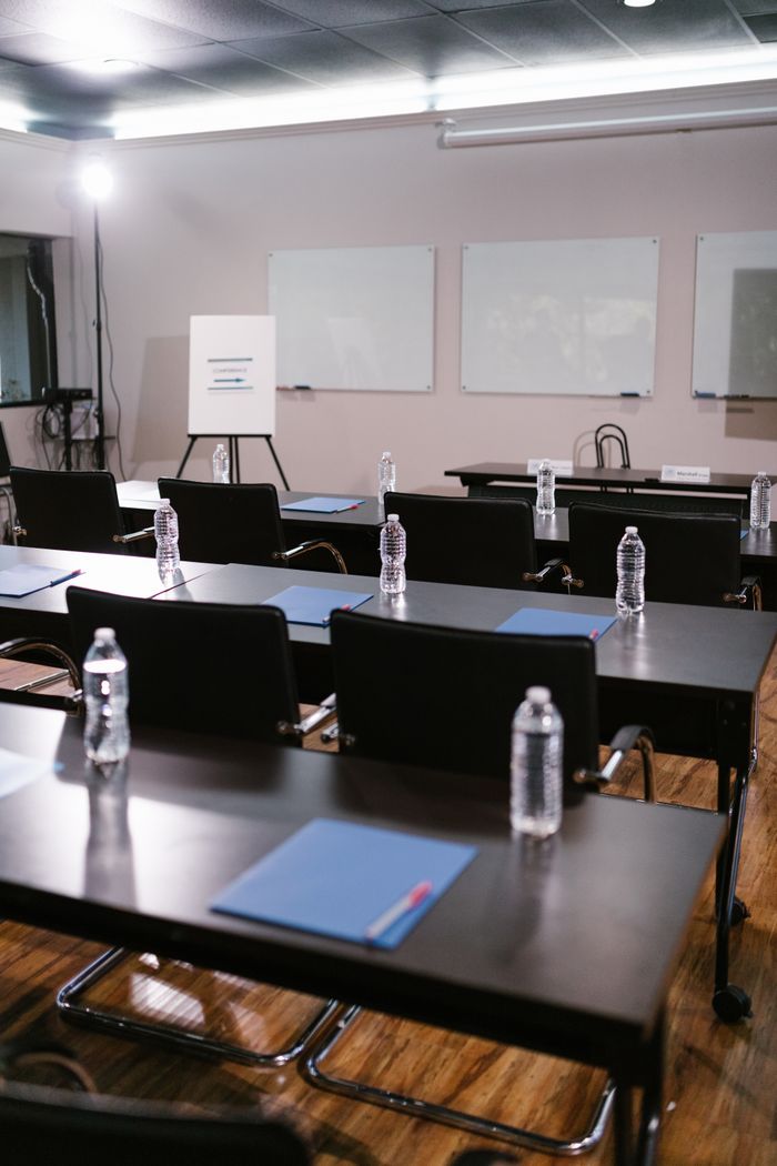 A neatly arranged conference room with tables, chairs, water bottles, and stationery ready for a meeting.