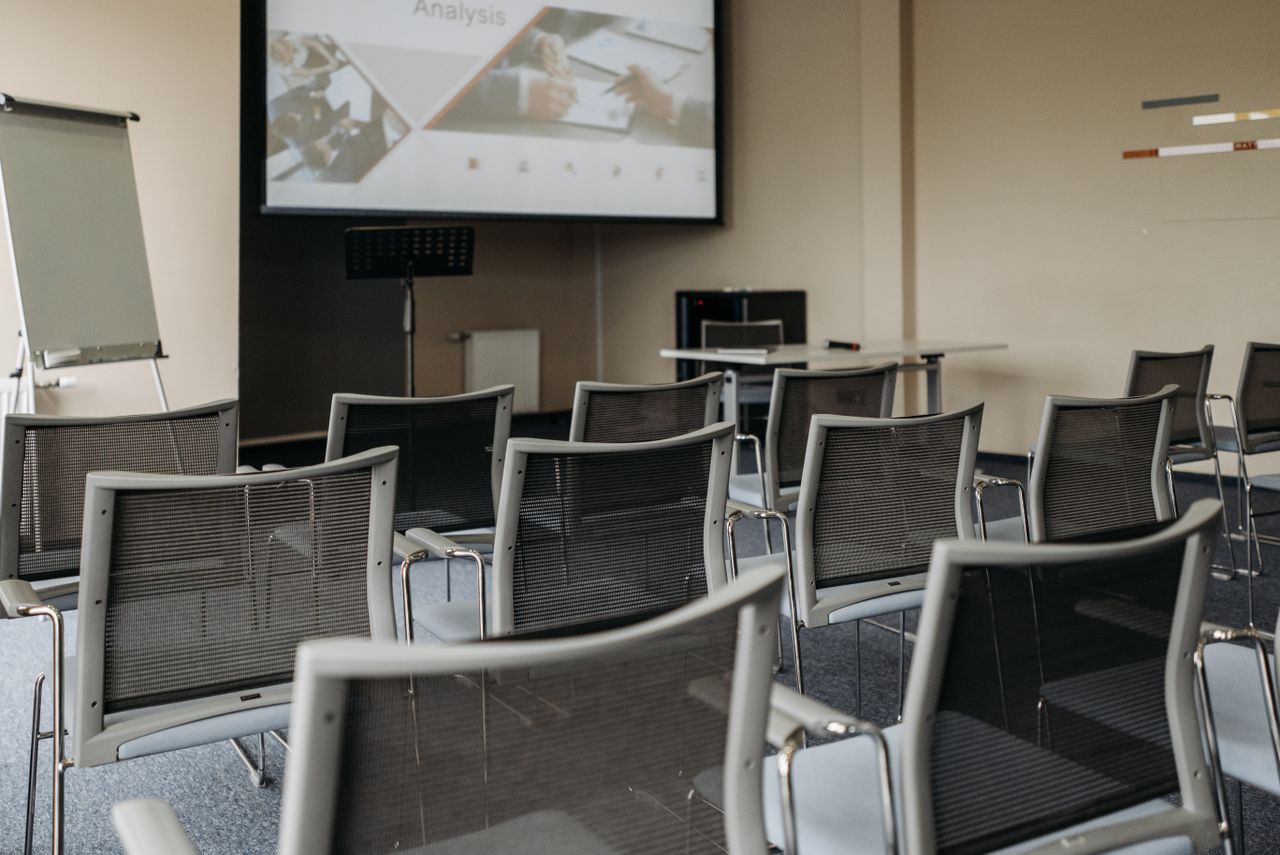 Modern conference room setup with empty chairs, projector screen, and presentation equipment.